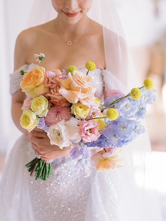 Bridal bouquet of pastel roses, hydrangea, and billy balls held by a bride in an off-the-shoulder sequin gown in soft indoor light