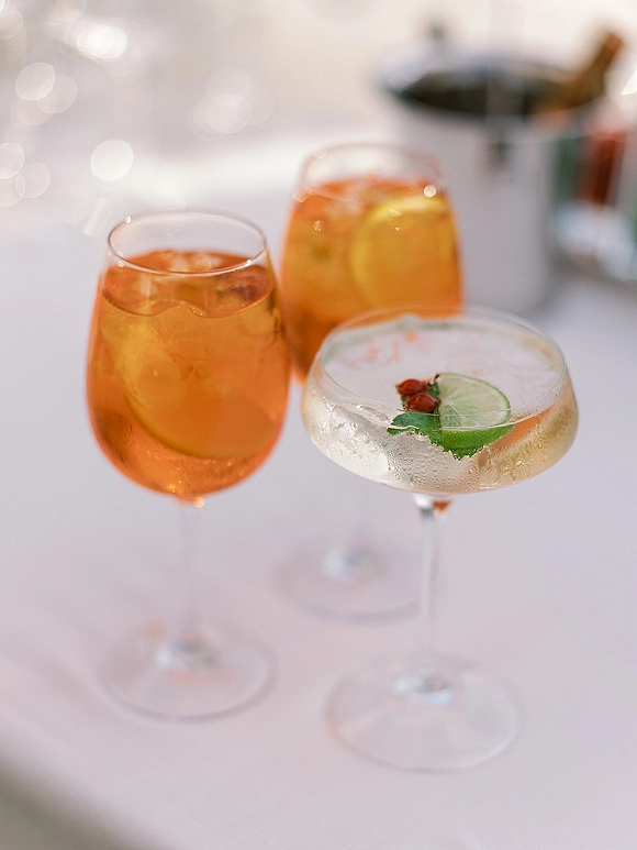 Wedding cocktails and wedding signature drink in coupe and stemless glasses with mint garnish on a white tablecloth beside bokeh lights