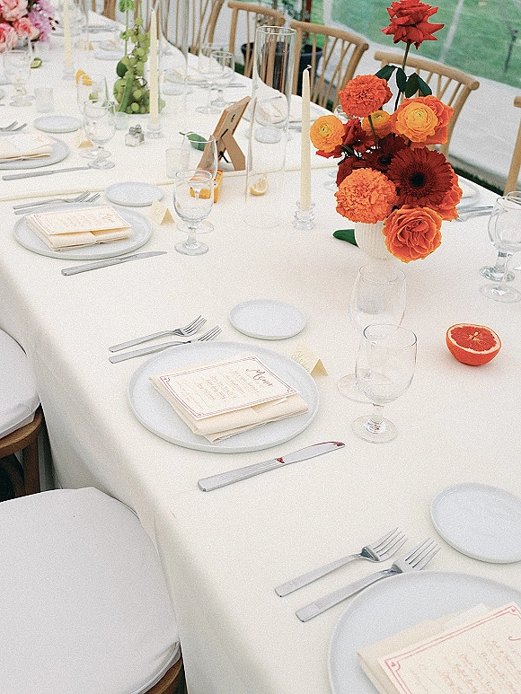 Reception tablescape with wedding table setting on a white tablecloth, taper candles, floral centerpiece, and grapefruit halves under a lawn tent