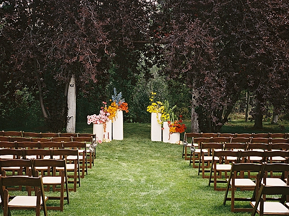 Outdoor ceremony setup with garden wedding ceremony seating, wood folding chairs lining an aisle with markers and floral plinths on a lawn amid trees