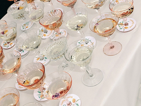 Wedding place cards and round wedding place cards with citrus illustrations beside champagne coupes and blush pink glassware on white linen table