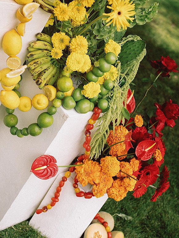 Wedding cake topped with fruit wedding cake styling, lemons and limes, marigolds and anthurium on a grass lawn backdrop
