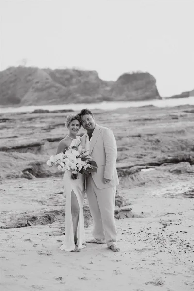 Couple portrait of bride and groom embracing at a beach wedding portrait, bride holding bouquet by rocky shoreline with ocean and cliffs behind