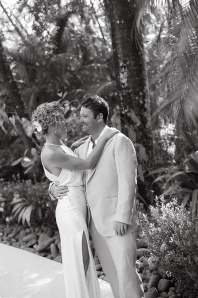 Couple portrait of bride and groom embrace, smiling as her halter slit gown stands out against tropical foliage and palms