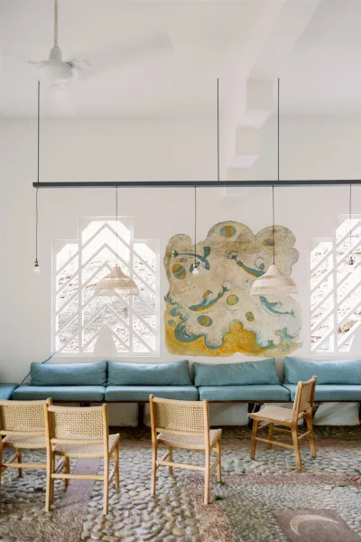 Ceremony seating with wedding chair setup of mixed wood and cane chairs flanking an aisle, lit by pendant bulbs in a white-walled room with arched windows