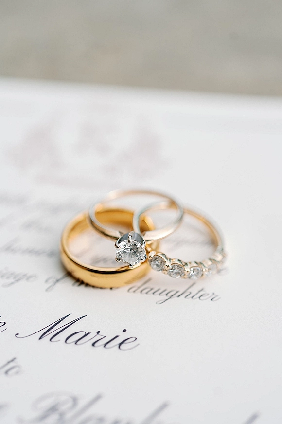 Wedding rings in a flat lay on wedding invitation paper, featuring a diamond engagement ring alongside gold wedding bands