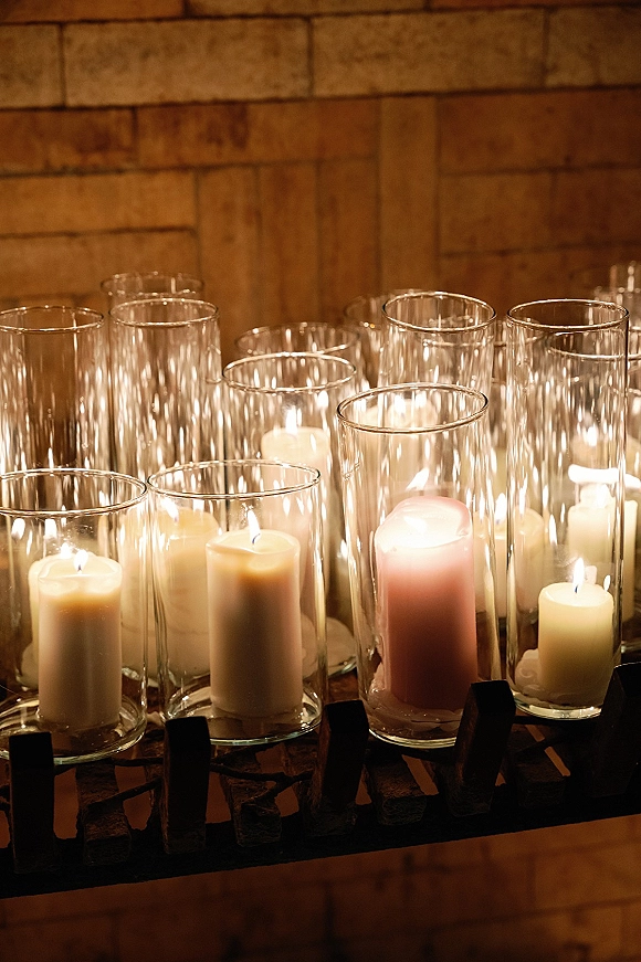 Wedding candle decor with glass hurricane candles and pillar candles in varied heights on a black metal stand against a brick wall