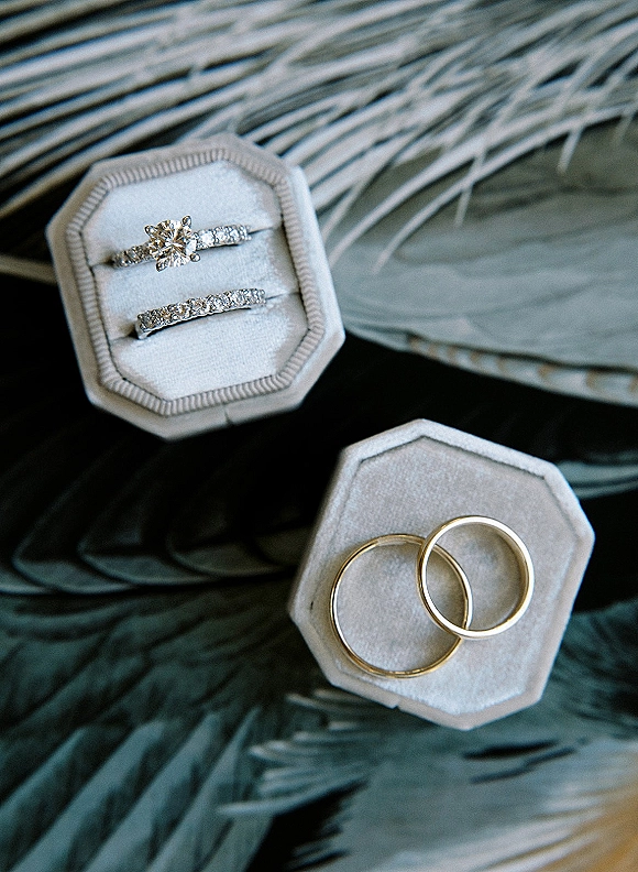 Wedding rings with a diamond engagement ring and band in a white velvet ring box, styled on palm leaves for a tropical detail flat lay