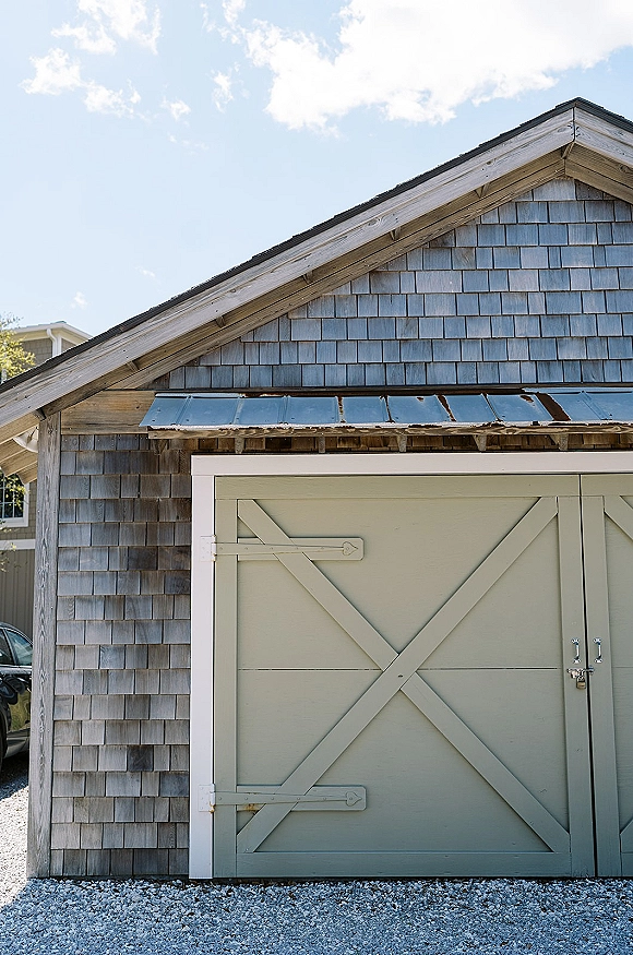 Barn doors with rustic barn doors styling, gray crossbuck sliding panels and metal hardware on shingle siding beneath a metal awning