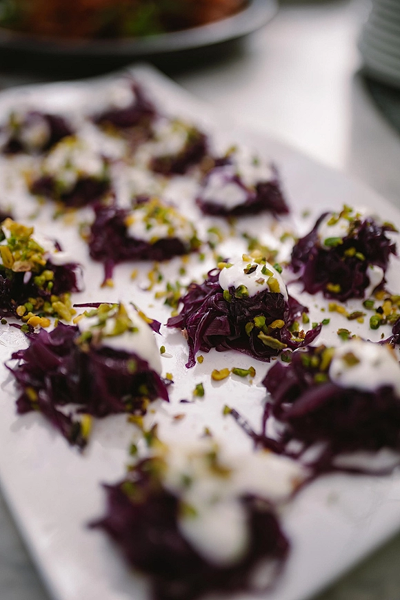 Wedding appetizers on a white serving platter with creamy topping, chopped pistachios, and shredded purple cabbage on a table surface
