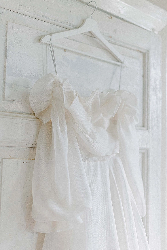 Wedding dress hanging on a dress hanger, strapless bodice with organza ruffles and tulle skirt against a white paneled door