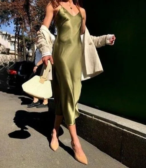 Olive satin slip dress with a cream coat over the shoulders on a city street