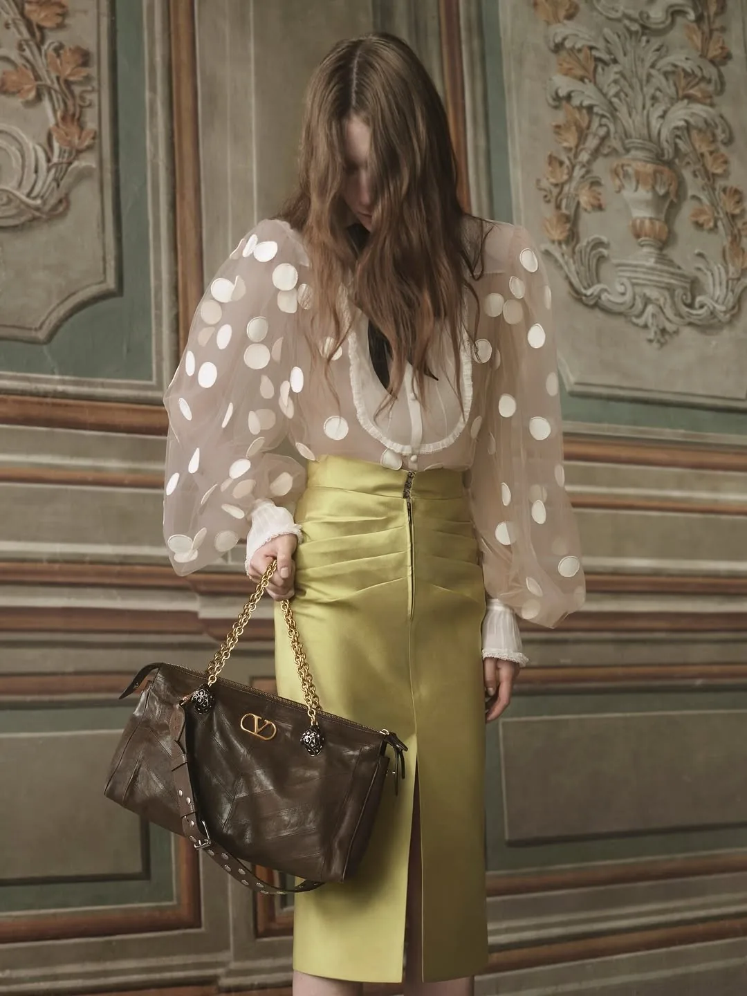Sheer polka-dot blouse over a chartreuse satin skirt with a brown leather bag