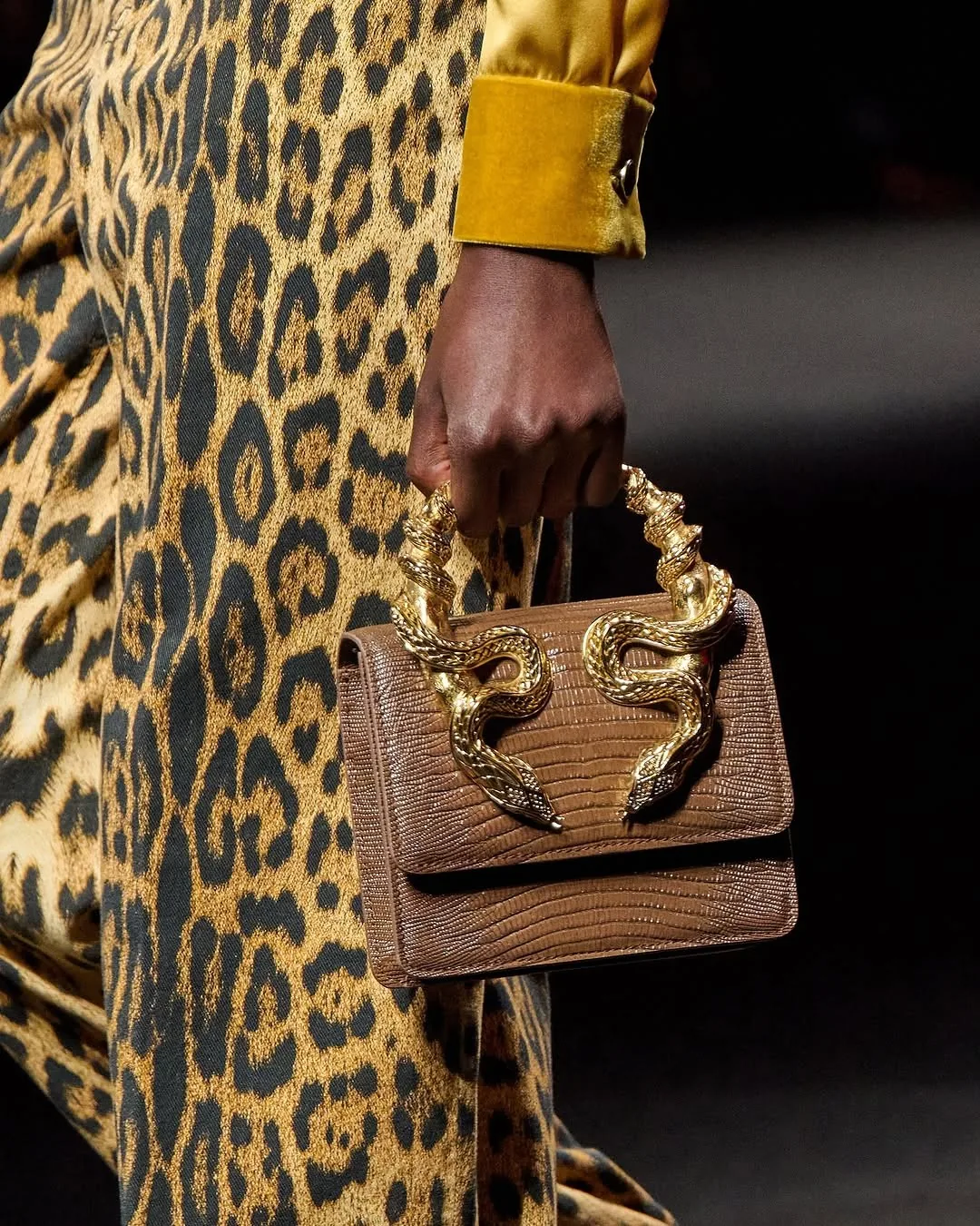 Brown croc-effect bag with gold serpent handles carried against a leopard-print coat