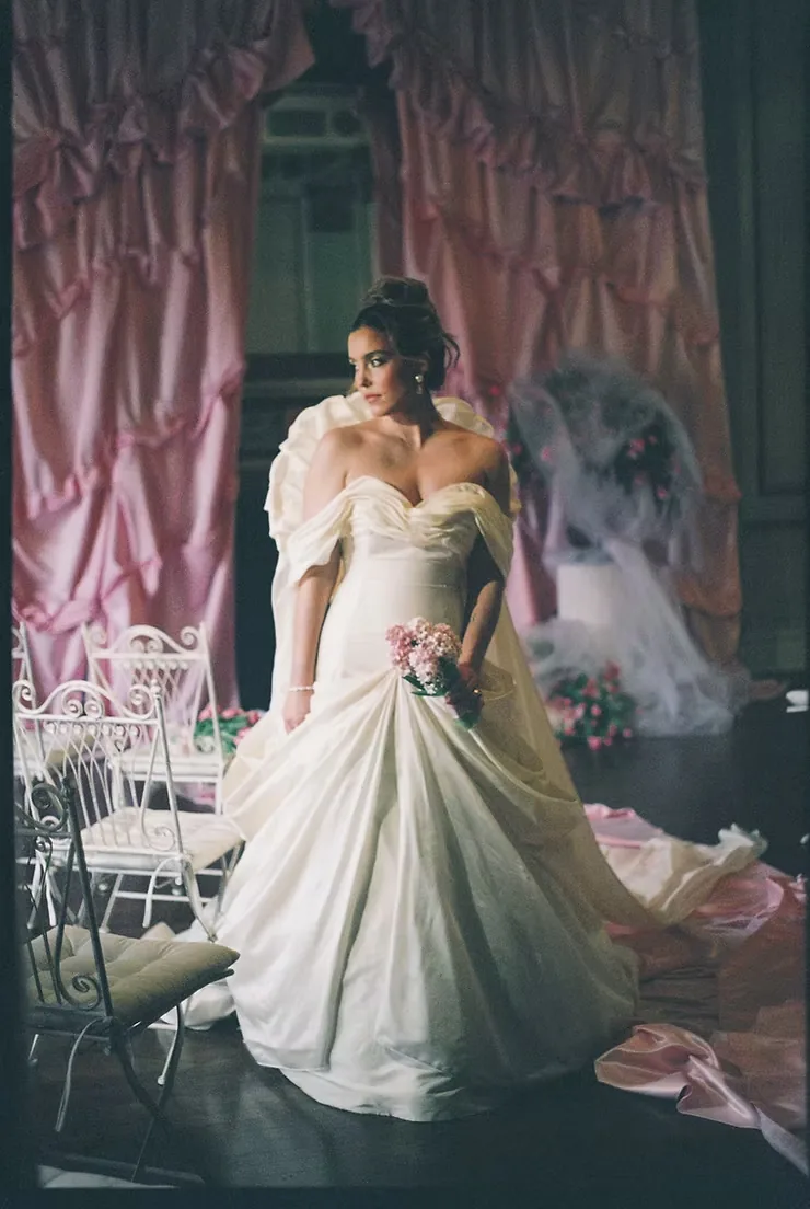 Bride in an off-the-shoulder ball gown in a gilded room hung with pink ruched drapery