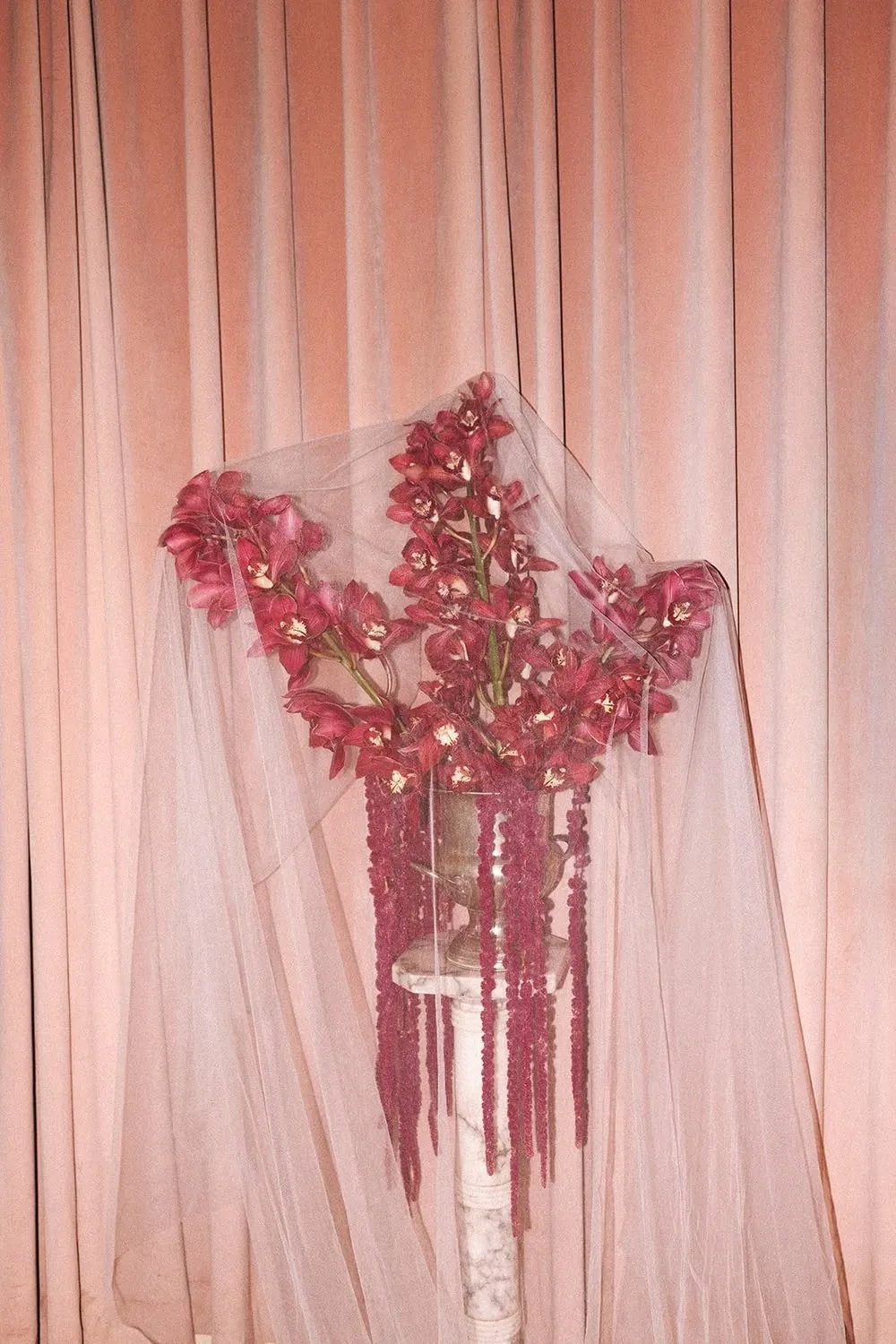 Pink orchid and amaranthus installation hung against sheer blush drapery