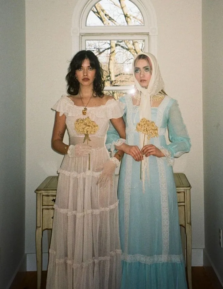 Two women in vintage lace dresses in pink and powder blue holding gold bouquets