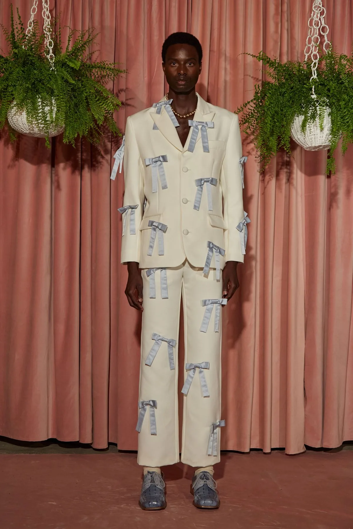 Ivory suit embroidered with blue bows against pink curtains