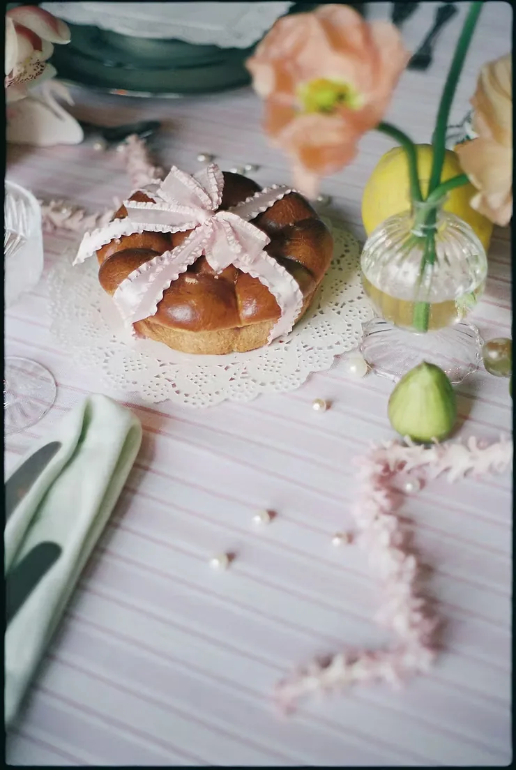 Brioche tied with pink ribbon on a lace doily beside poppies and pearls