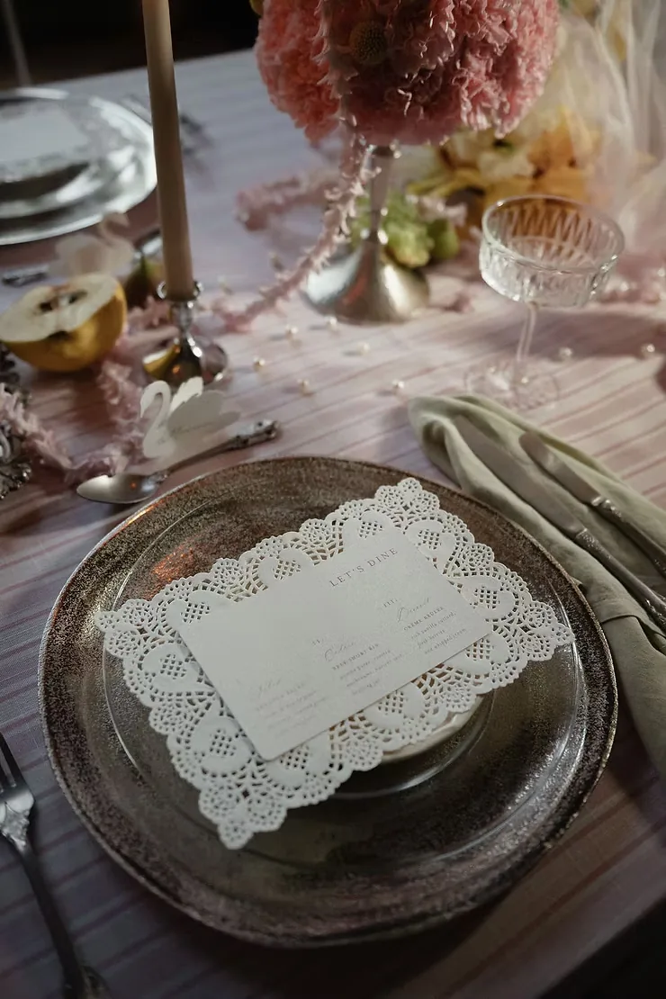 Place setting with a paper doily menu, silver charger and pears