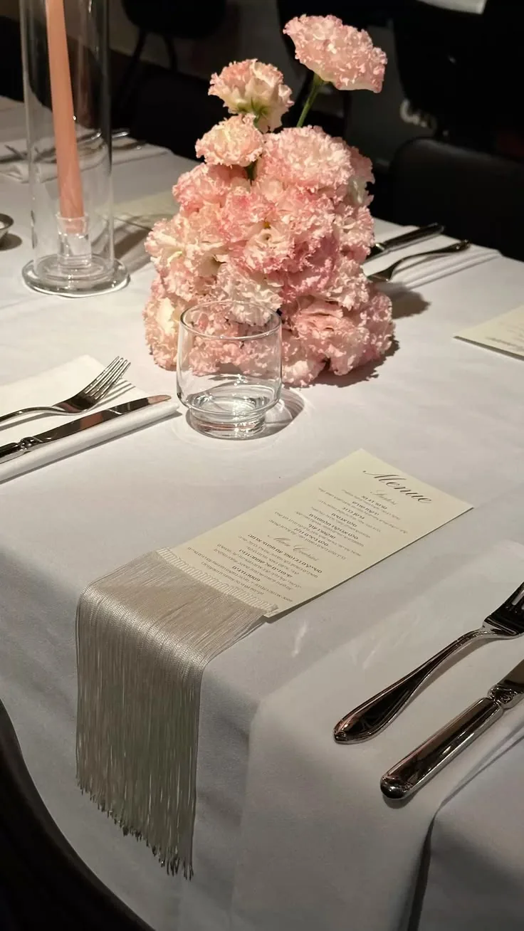 Pink carnation centerpiece on a white table with a fringed runner