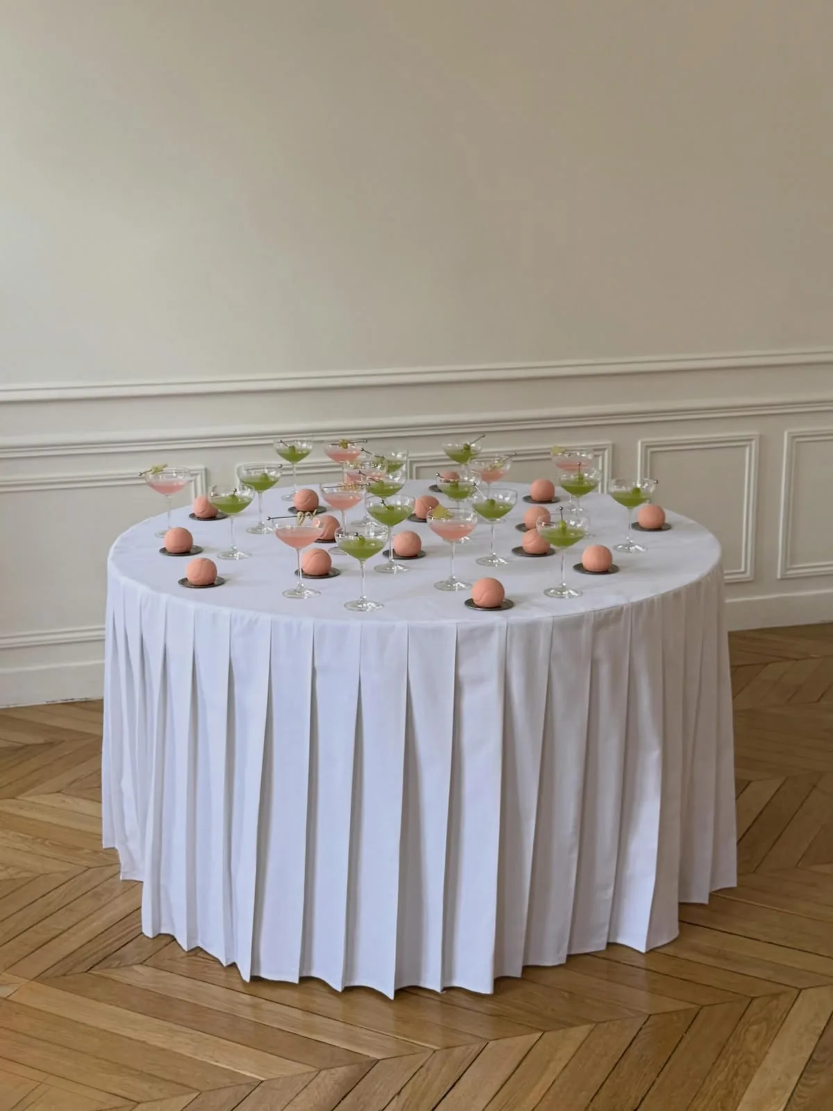 Round table with a pleated white skirt set with pink desserts in a paneled room