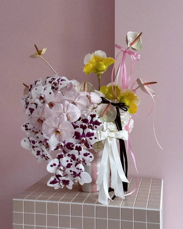 Phalaenopsis orchid and yellow bloom arrangement tied with ribbons on a pink tiled plinth