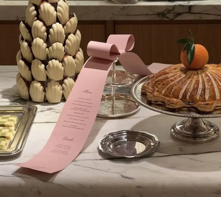 Madeleine tower with a pink ribbon menu beside a tart on silver trays