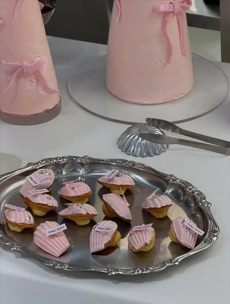 Pink cone cakes tied with bows beside a silver tray of pink madeleines