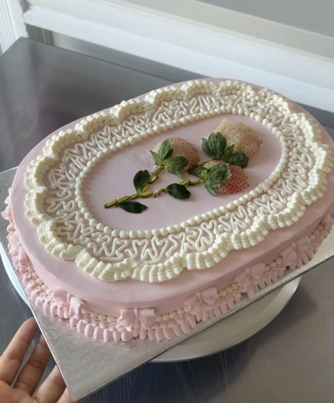 Pink oval cake piped with cream ruffles and topped with strawberries