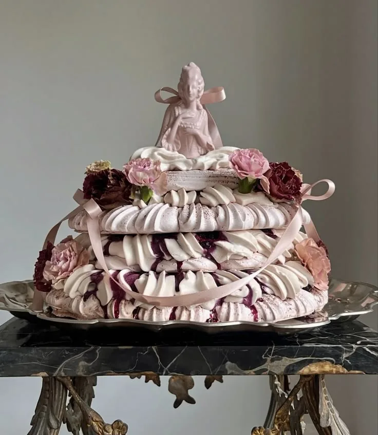 Pink meringue cake topped with a porcelain figurine and roses