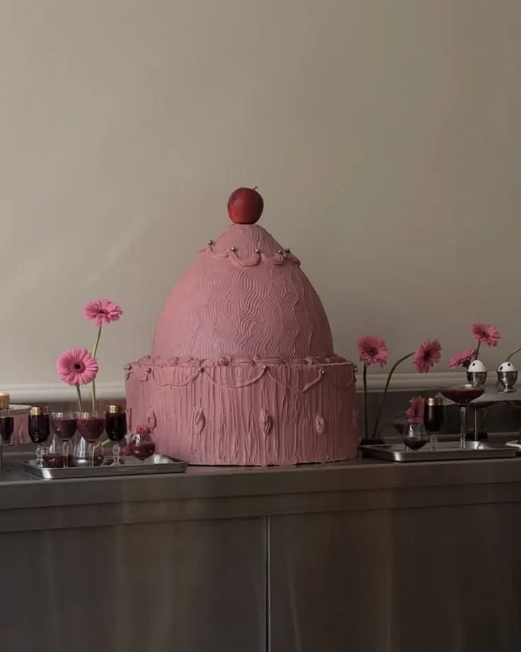 Pink domed cake topped with a cherry on a steel counter