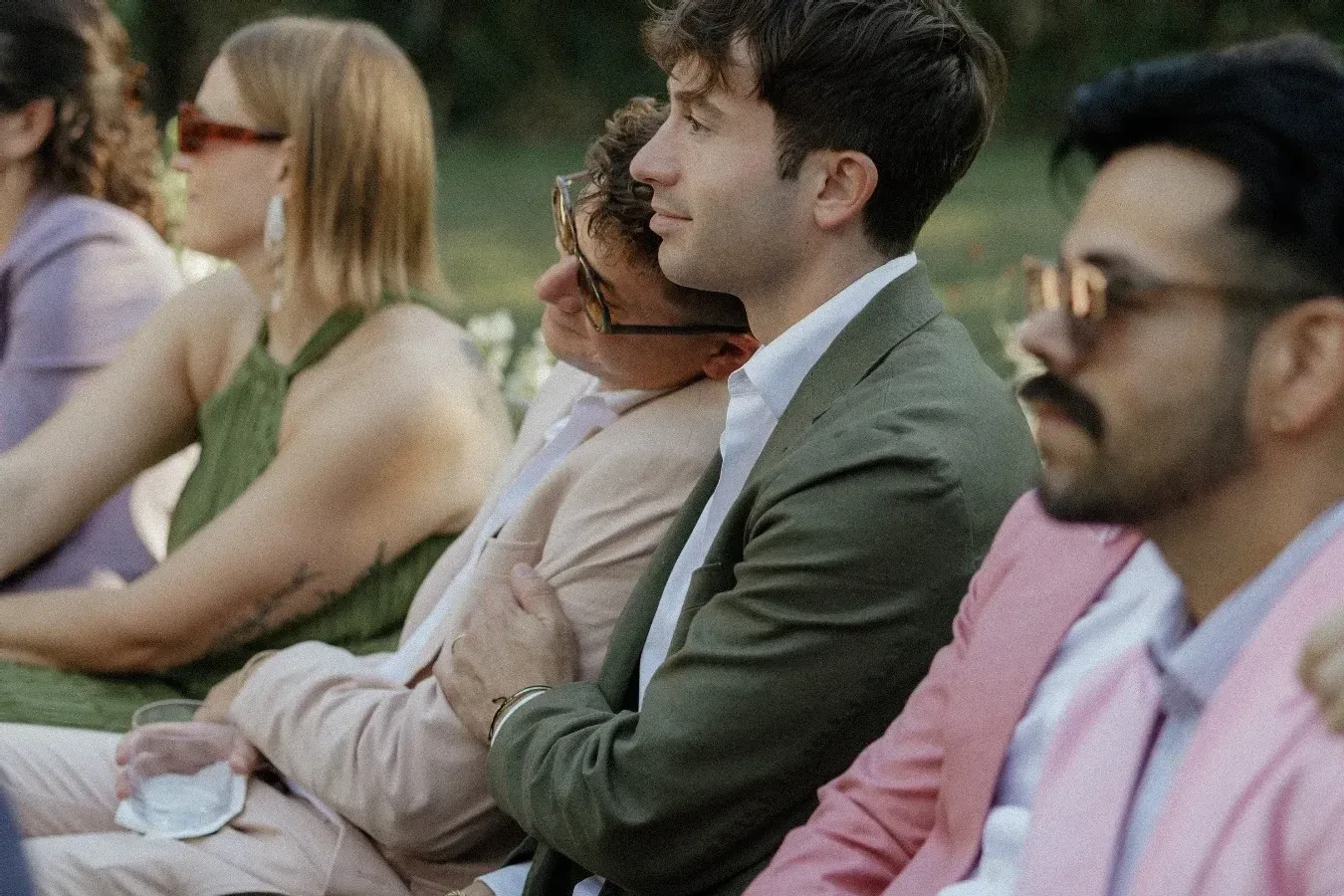 Several male guests watching a wedding ceremony in lightly colored suits. 