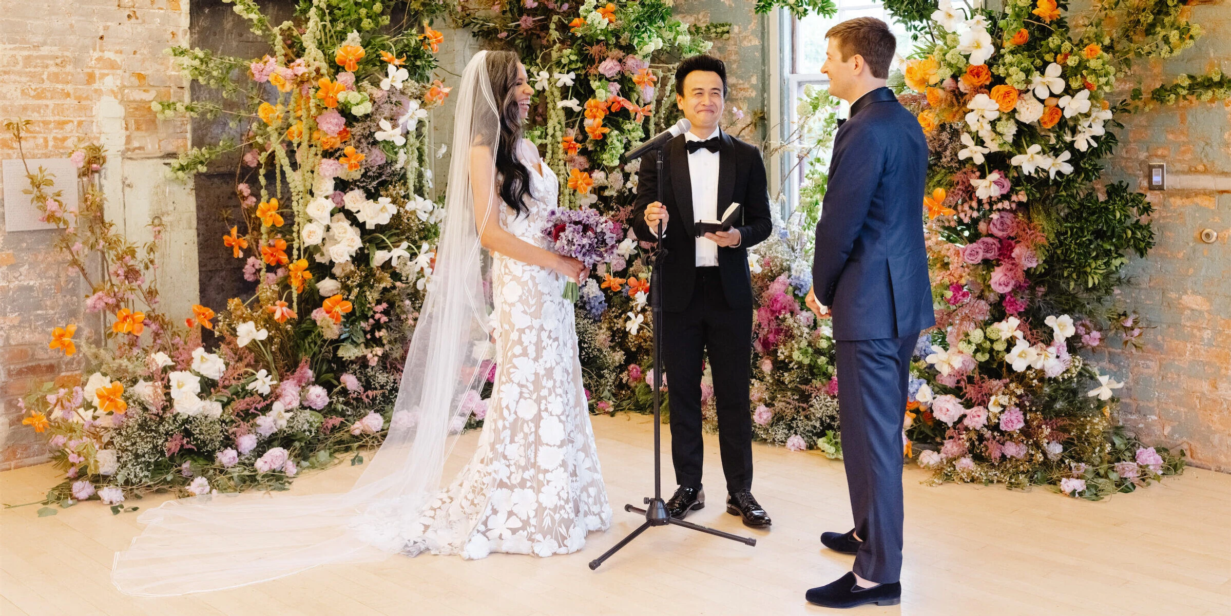 A bride and groom laugh during their flower-filled art museum wedding ceremony.