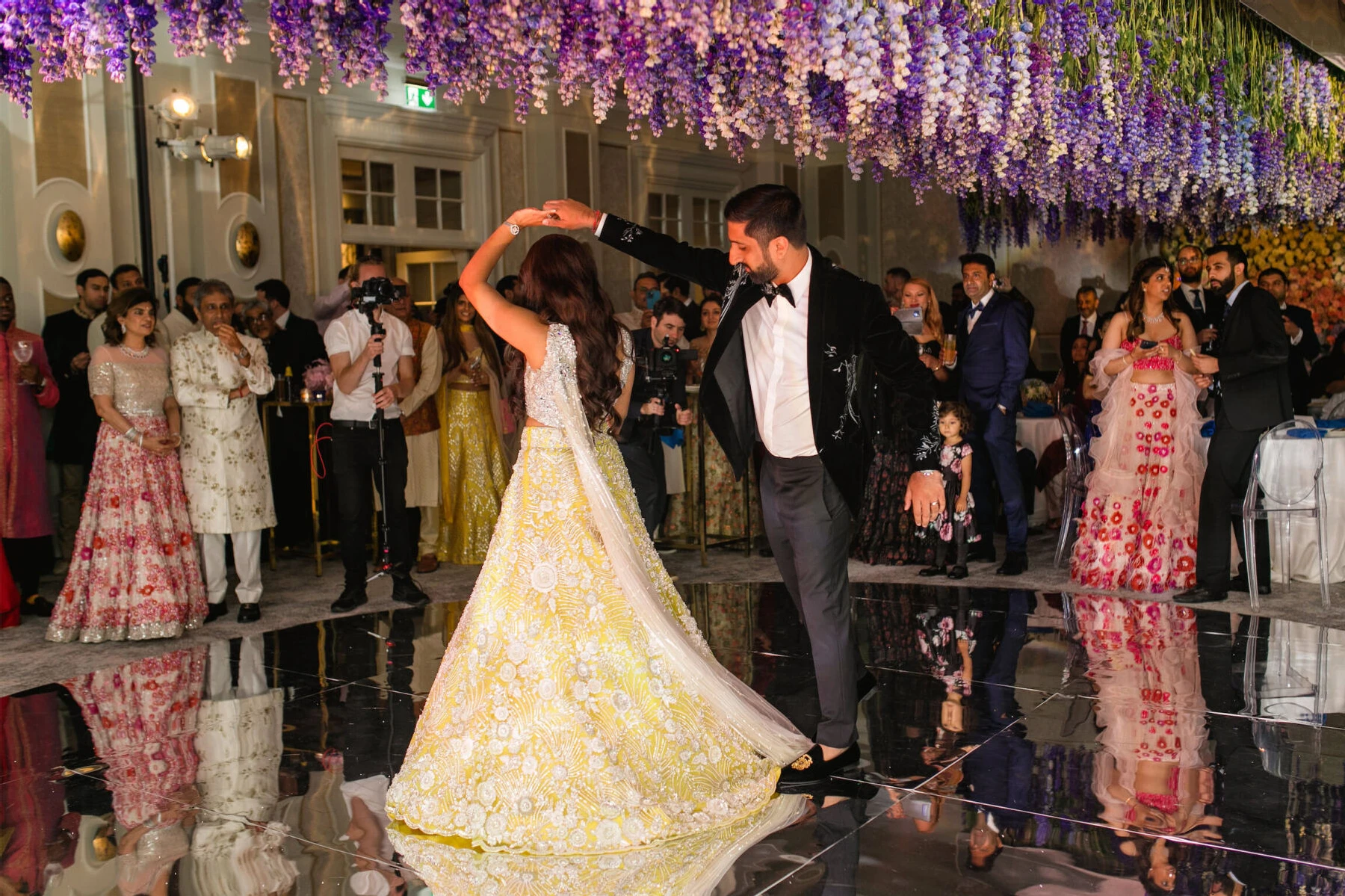 Newlyweds dance under an installation of delphinium flowers at their colorful countryside wedding in the ballroom of the Four Seasons Hampshire.