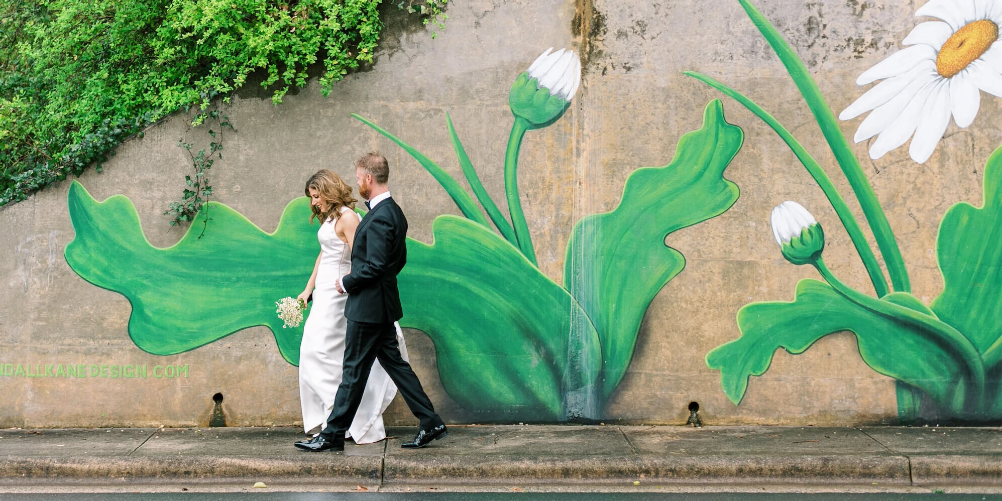 A bride and groom walk by a colorful, floral mural in North Carolina.