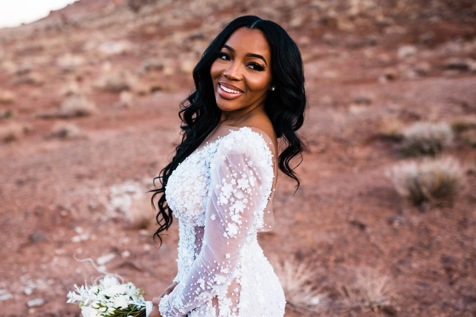 A smiling bride with soft waves and a natural makeup look at her desert wedding.