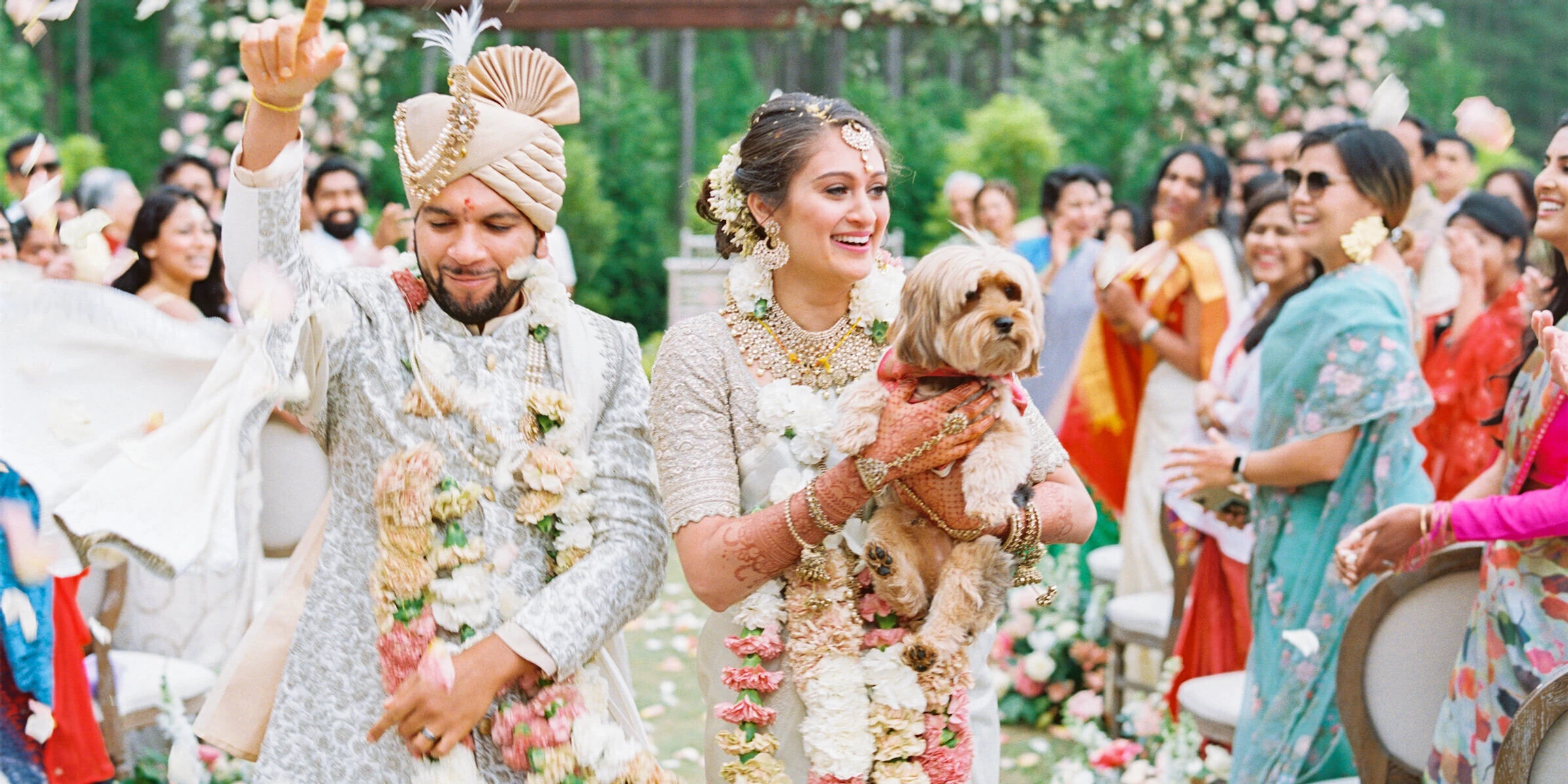 Newlyweds and their beloved pup recess up the aisle amidst a shower of rose petals at the end of their destination Indian wedding ceremony.