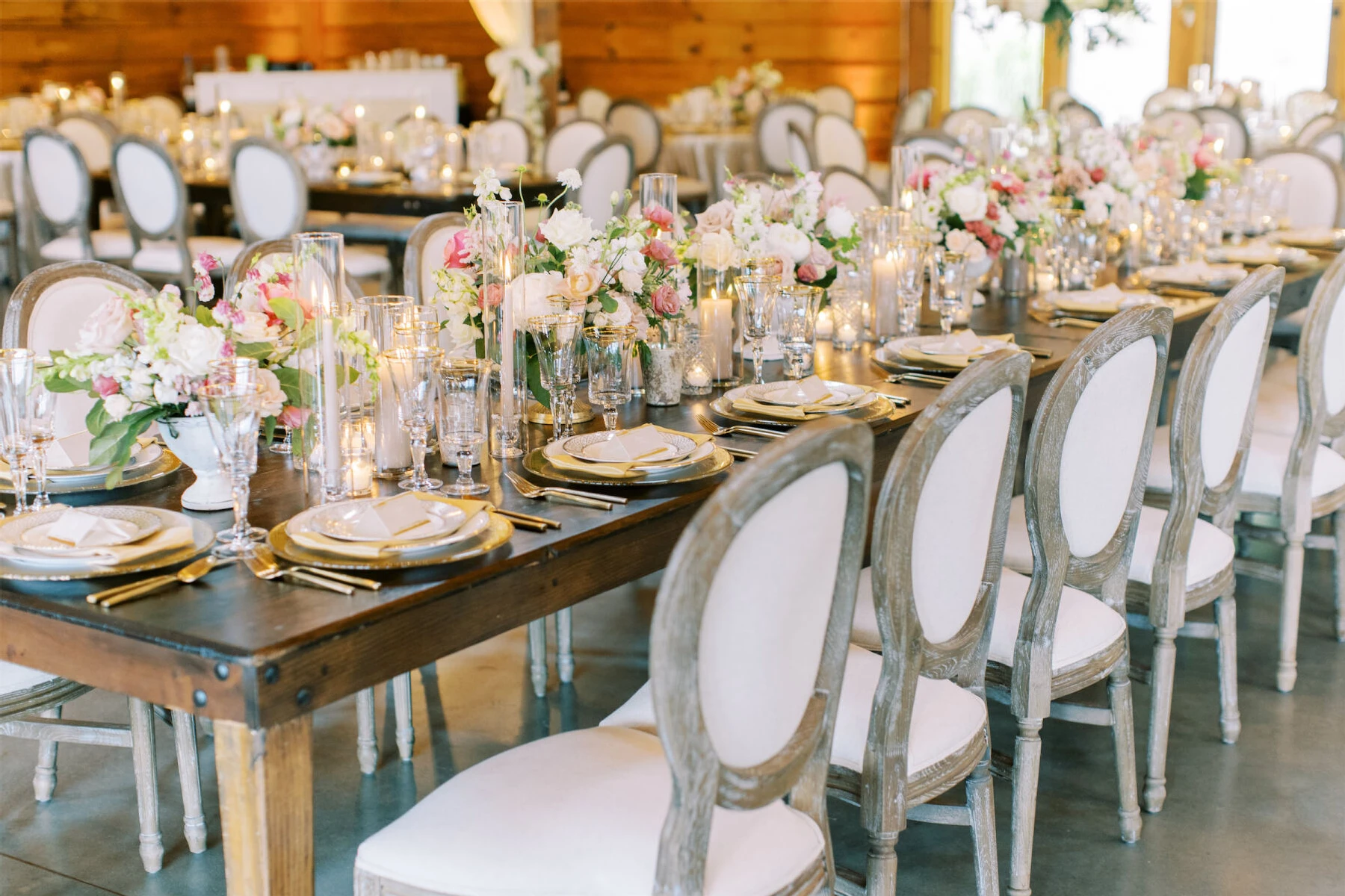 A beautiful reception was set inside a barn at this destination Indian wedding. Pink and white centerpieces decorated the tables, which were set with elegant, upholstered chairs.