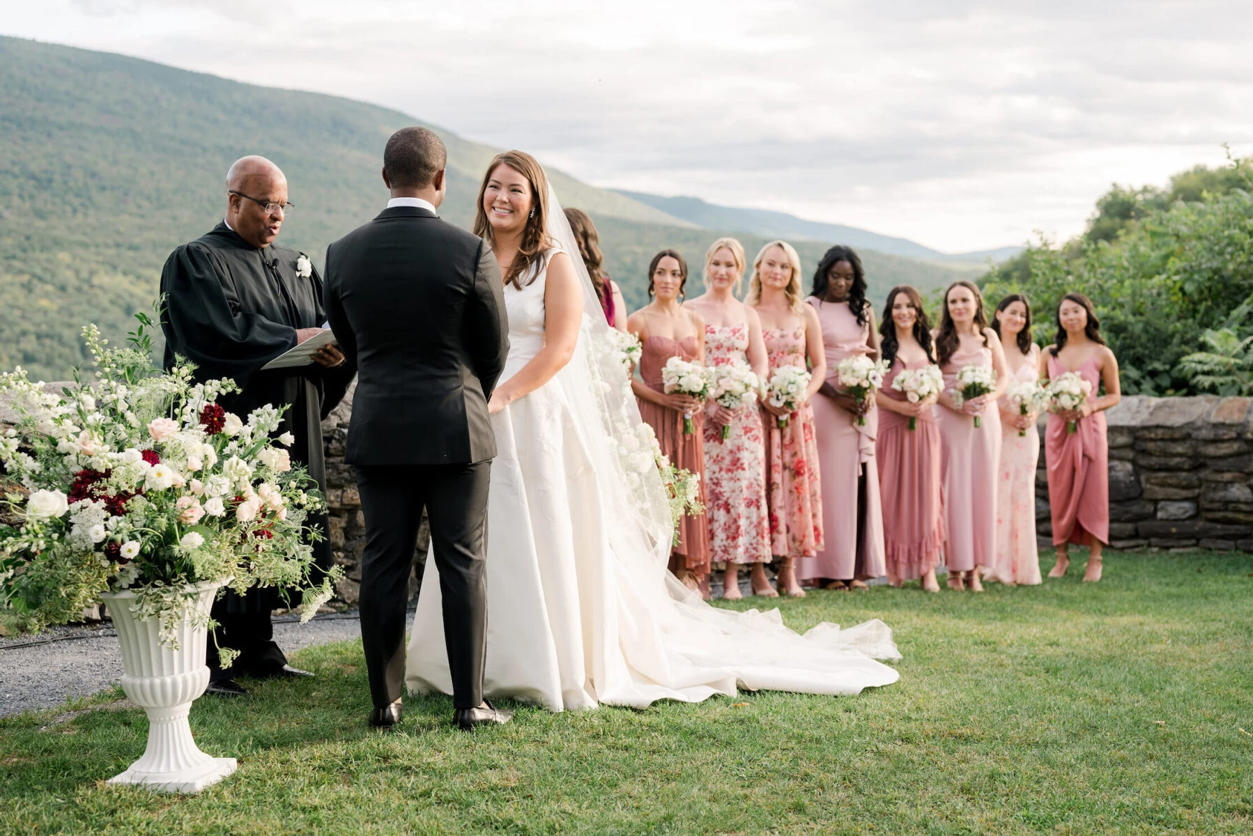 A bride looks at her groom during their elevated garden wedding ceremony, with views of the Vermont landscape, and the adoring eyes of her bridesmaids behind them.