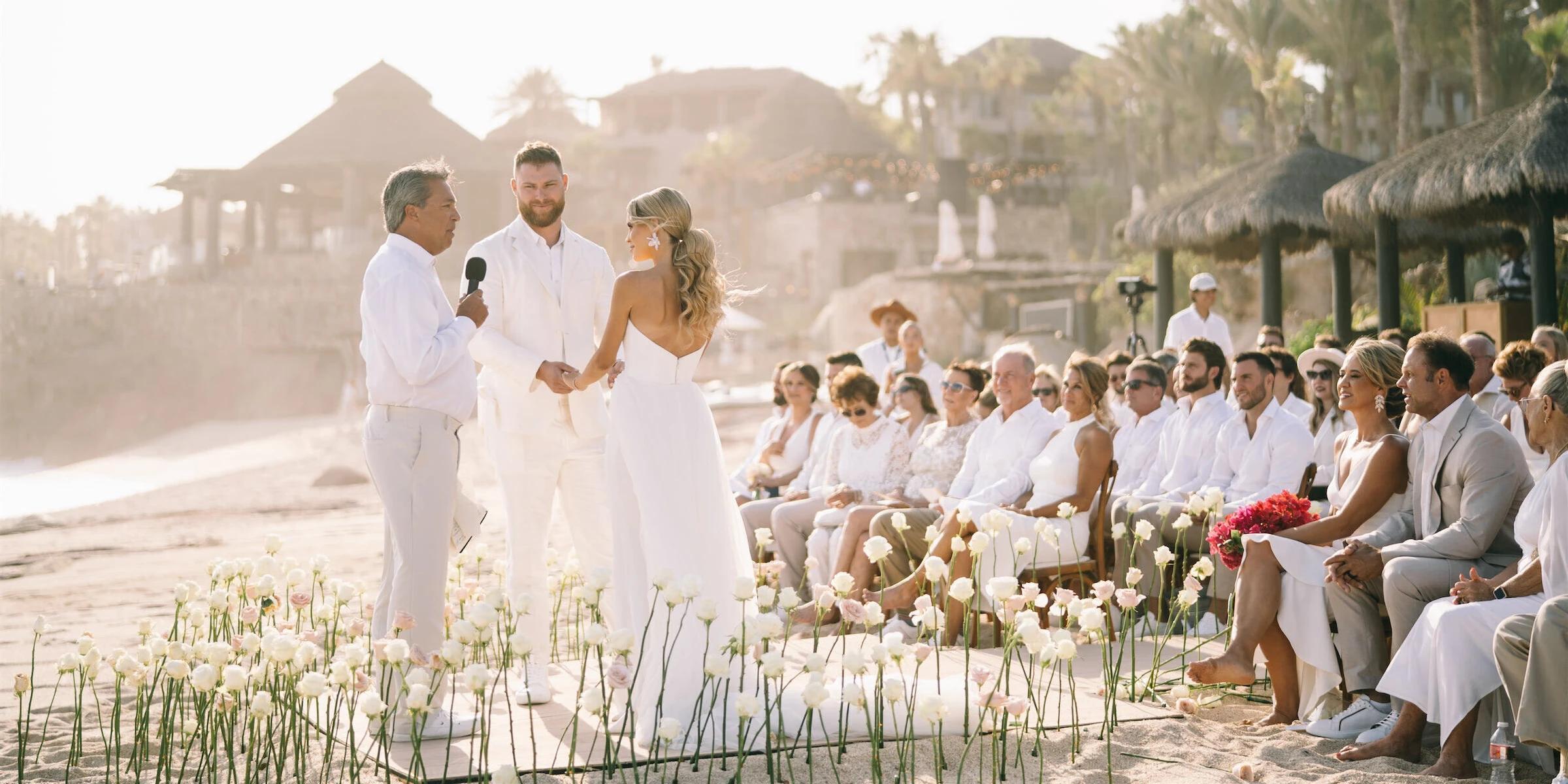 A glam beach wedding ceremony, with the couple surrounded by white roses seemingly growing out of the sand.