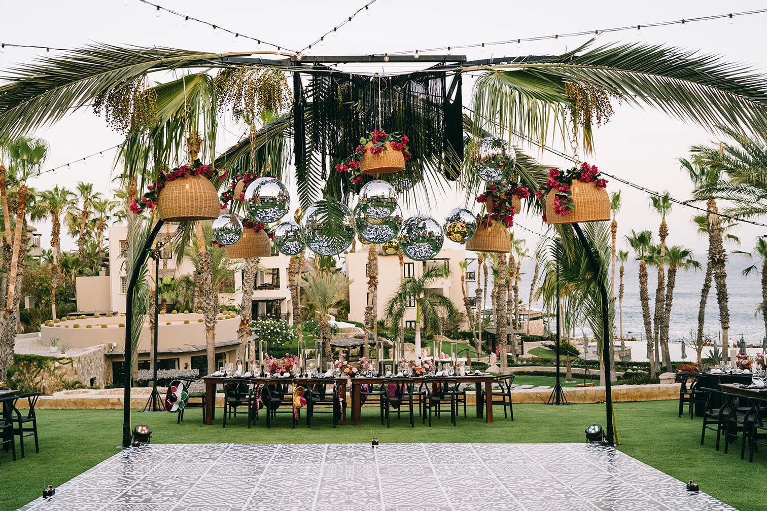 A glam beach wedding reception gave waterfront views and a fun, party vibe, courtesy of disco balls, woven light fixtures, and palm trees over a faux-tile dance floor, surrounded by the tables set for 75 guests.