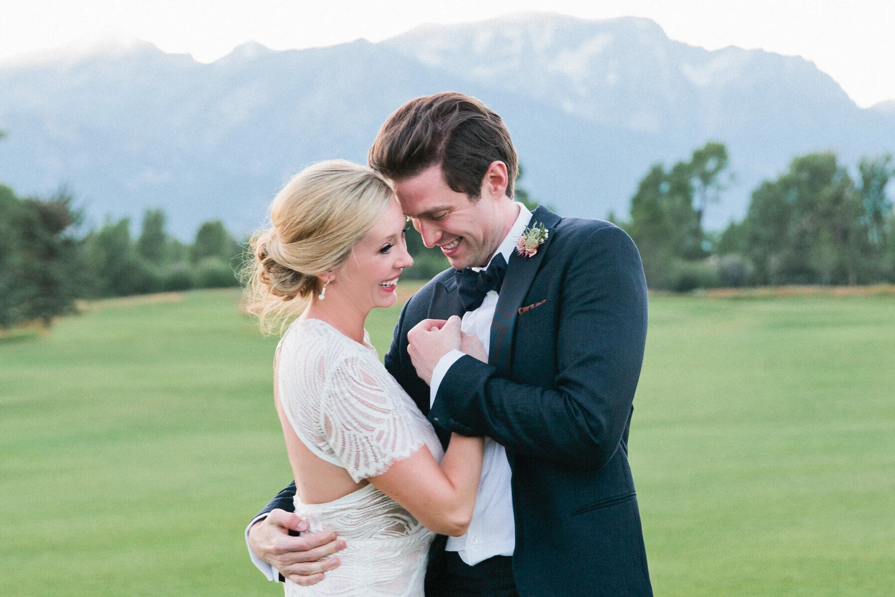 Golf Course Wedding Venues: A bride and groom embracing on their wedding day on a golf course with a mountain view.