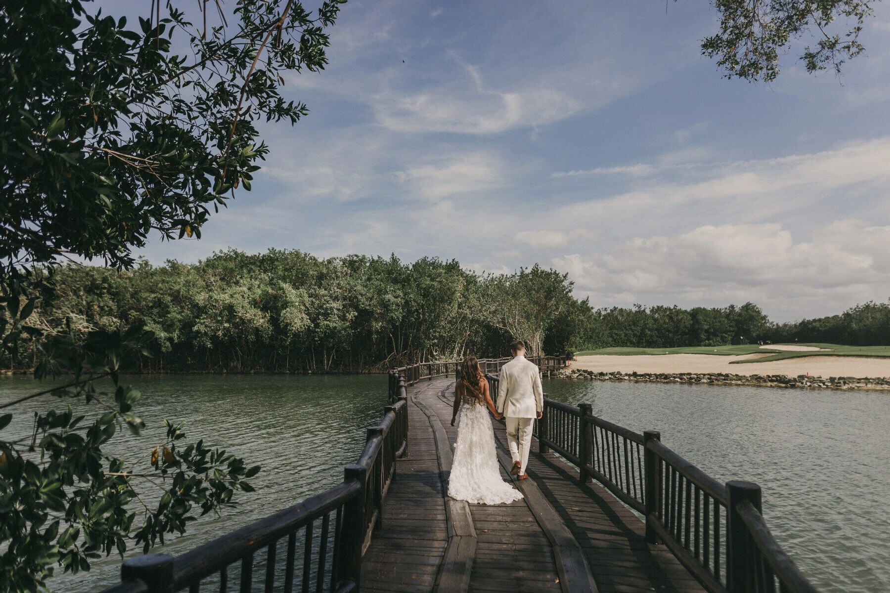 Golf Course Wedding Venues: A wedding couple holding hands while walking over a bridge.