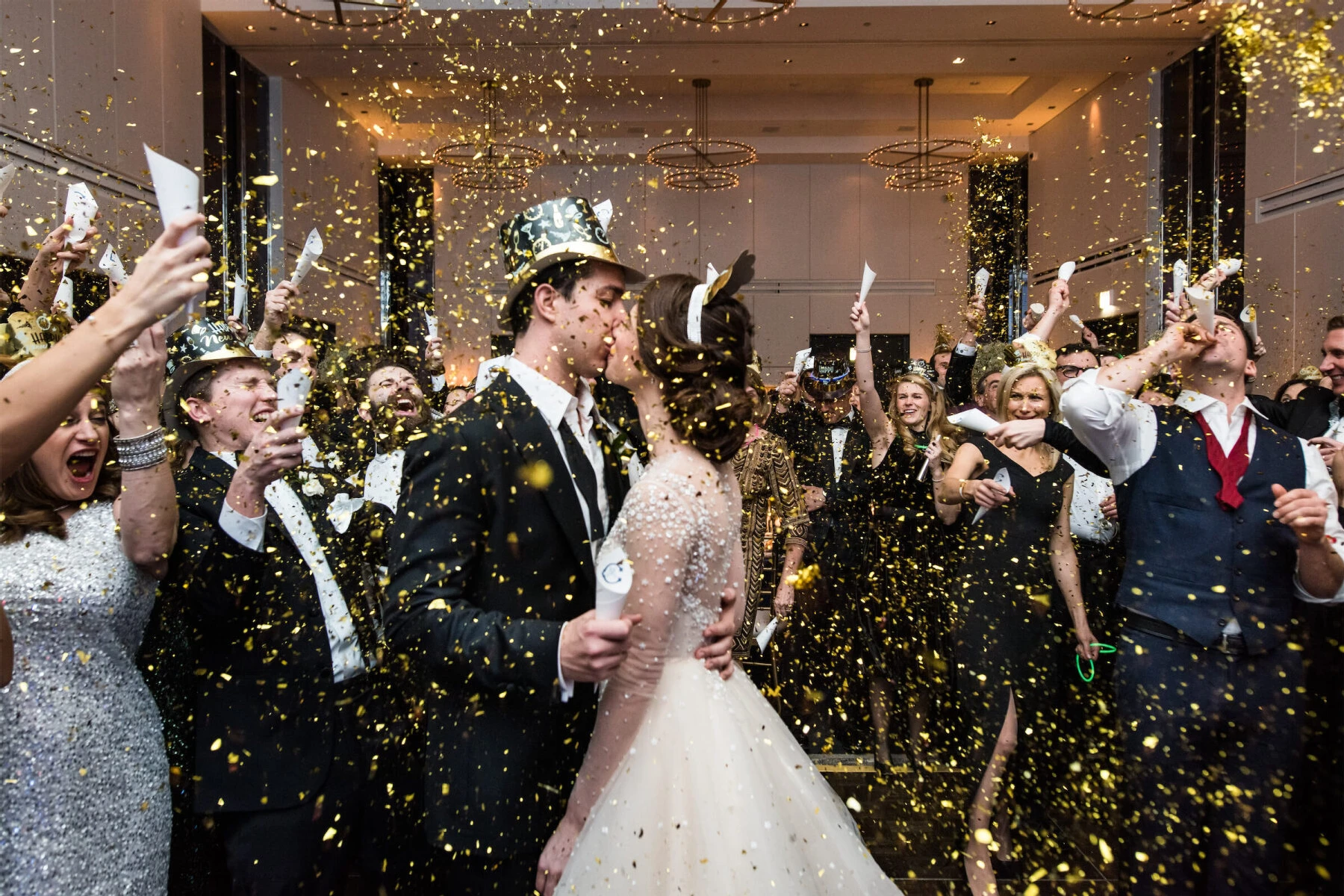 Holiday Wedding: A bride and groom wearing New Year's Eve accessories and kissing while loved ones throw confetti and cheer around them.