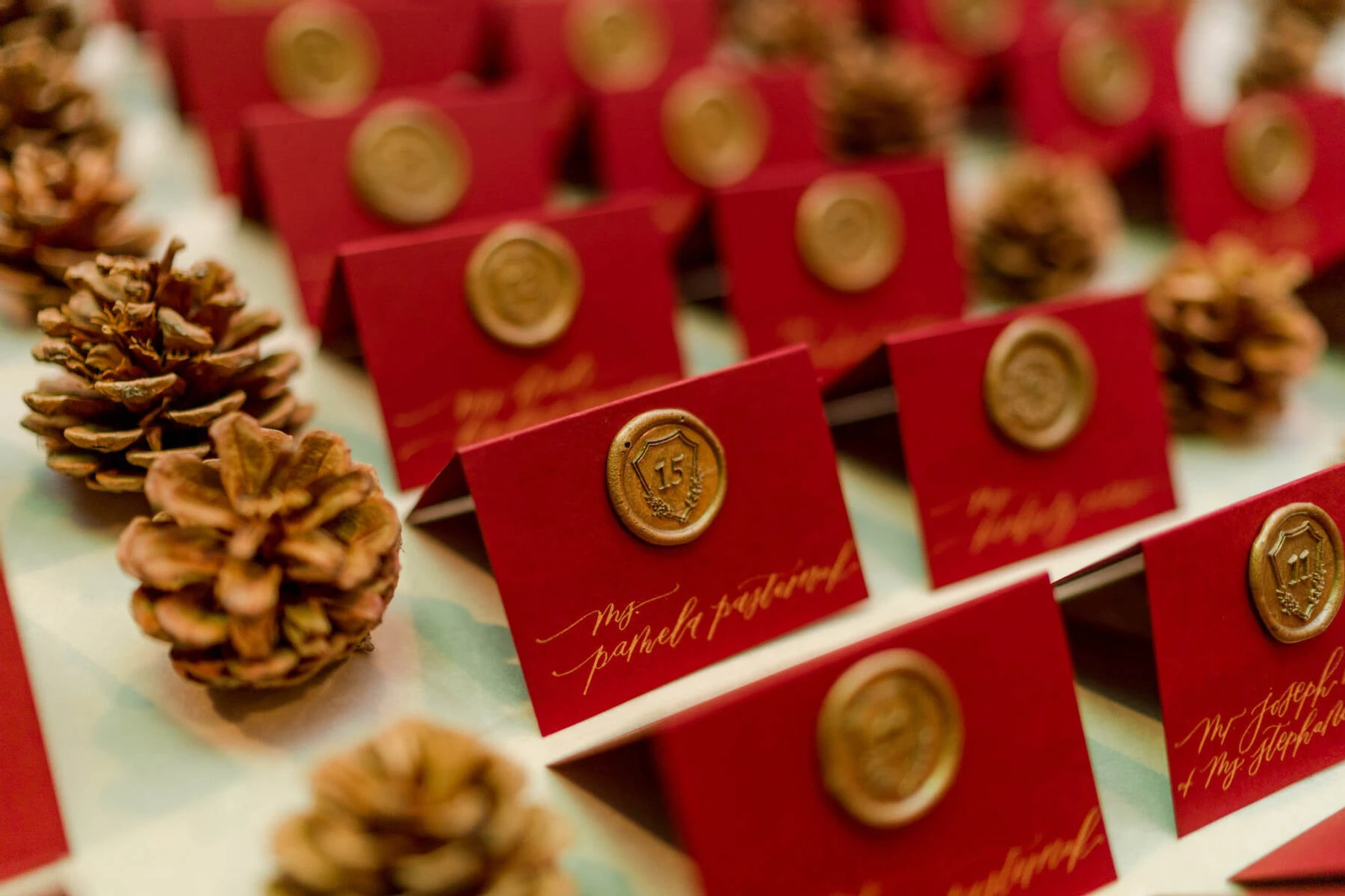 Holiday Wedding: Red seating escort cards stamped with table numbers in a wax seal. Pinecones are sitting next to the escort cards.