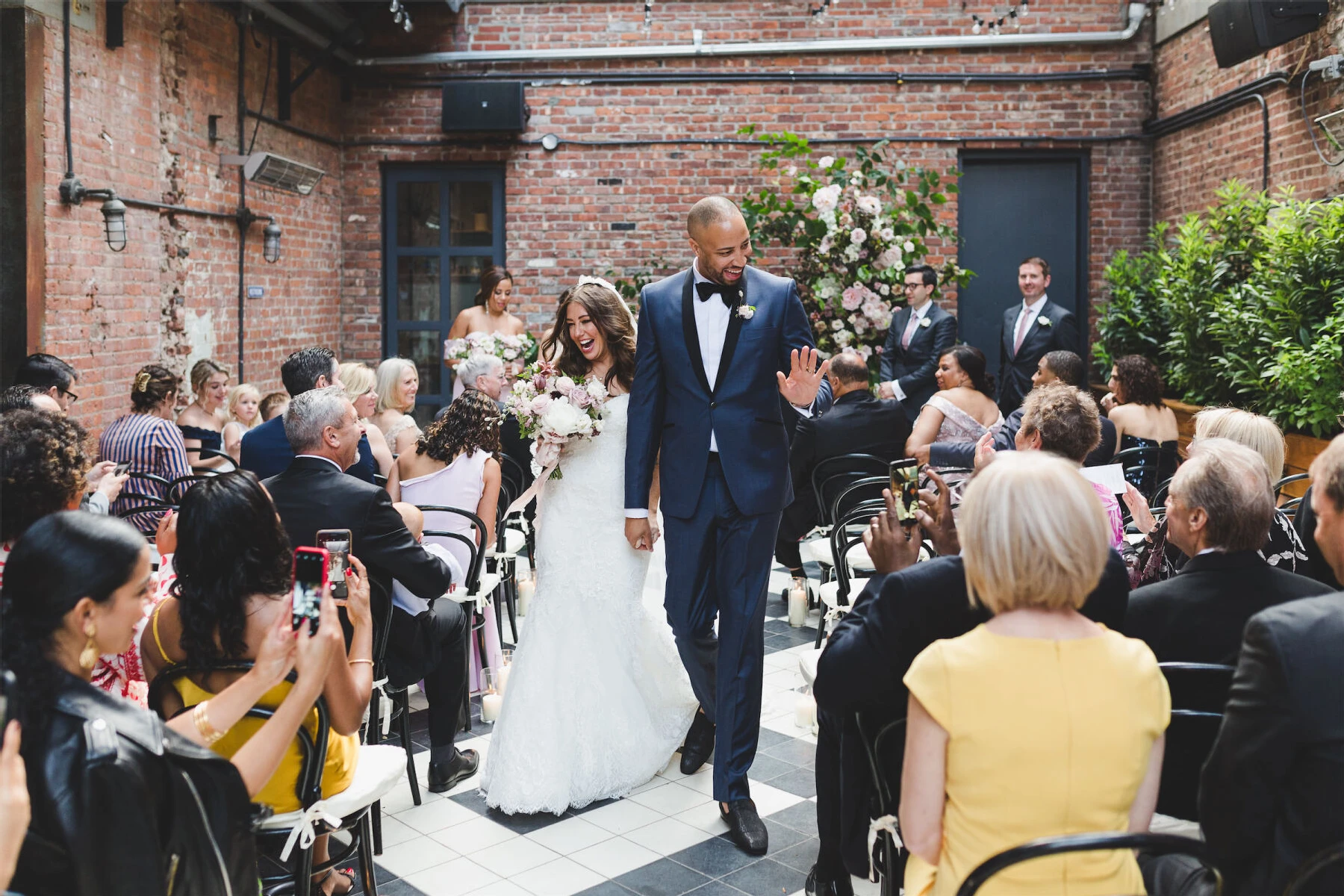 Holiday Wedding: A newly married couple walk back down the aisle together while holding hands and smiling at guests in the audience.