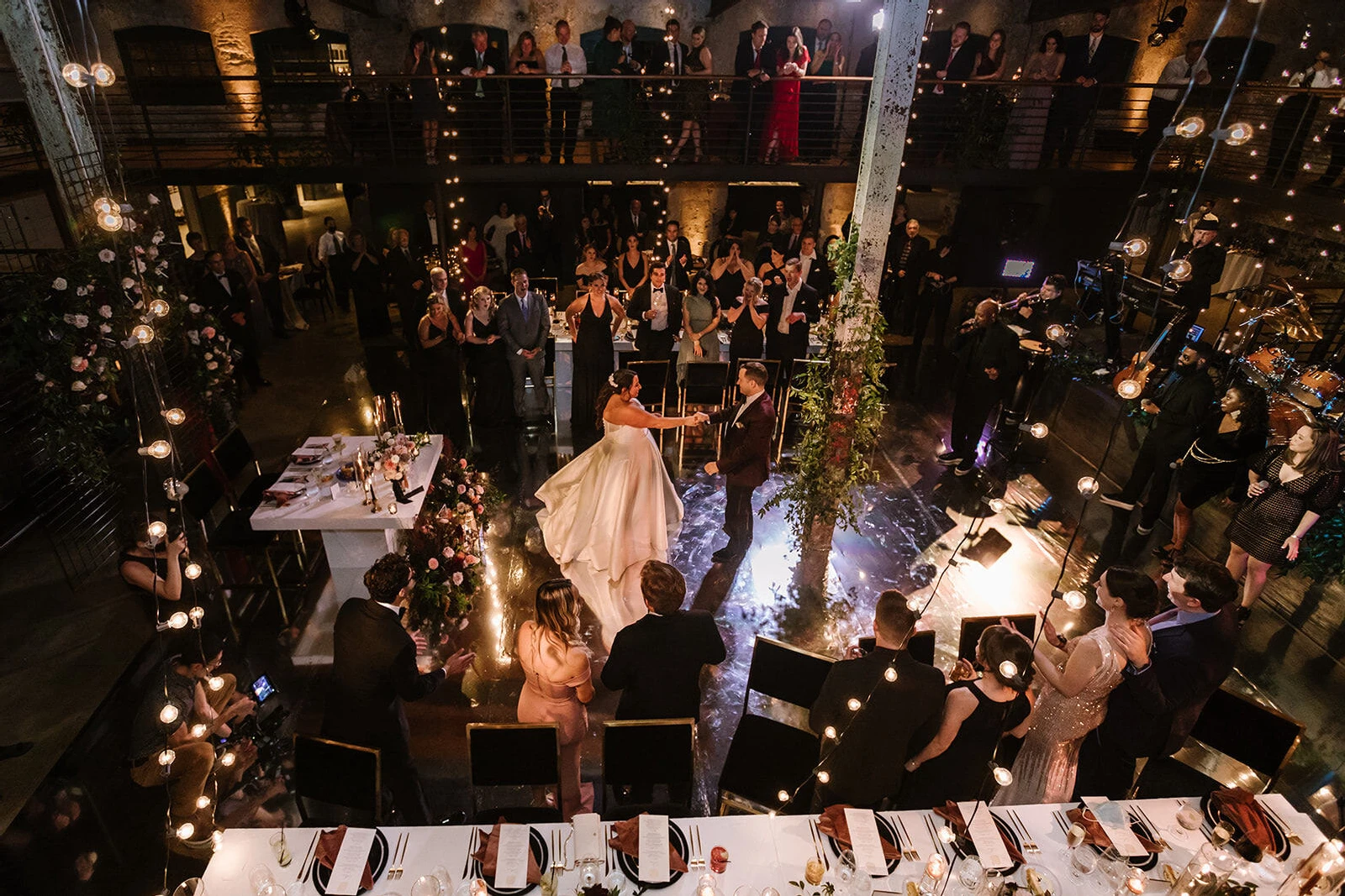 An overhead view of a reception space for an industrial wedding, with newlyweds dancing as their live band performs and guests surround them.