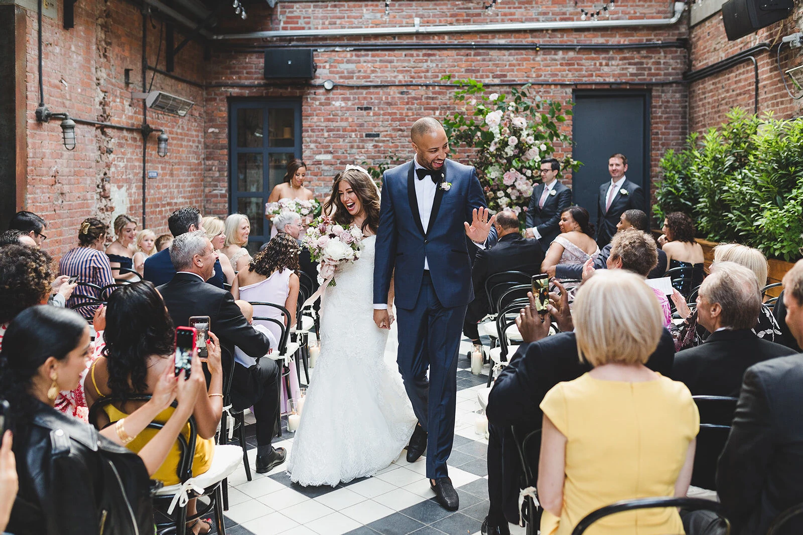 Industrial Wedding Venues: A bride and groom smiling, holding hands, and walking back down a narrow aisle together at Wythe Hotel.