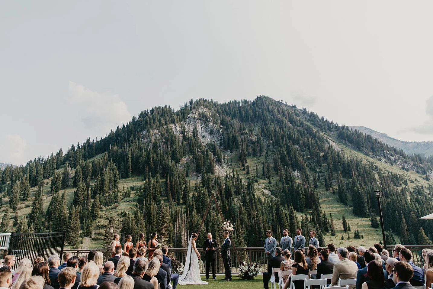 Mountain Wedding: A couple getting married in an outdoor ceremony, complete with a triangular wooded arch at the altar and mountains in the background.